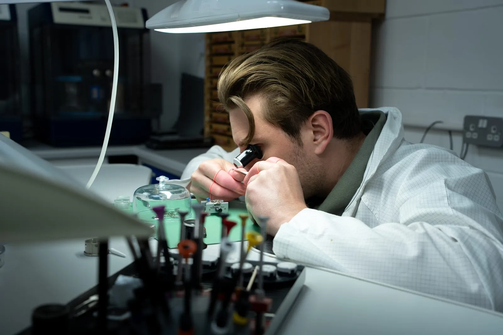 Senior SwissMade watchmaker working under the bench lamp with a loupe