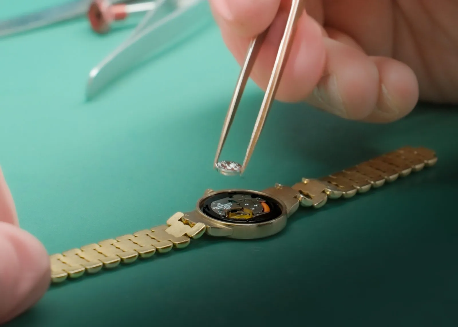 SwissMade watchmaker fitting a new battery into a gold watch with tweezers