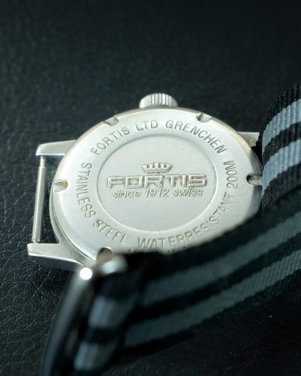 Engraved caseback of a Fortis Flieger on a striped NATO strap, ready for restoration at SwissMade