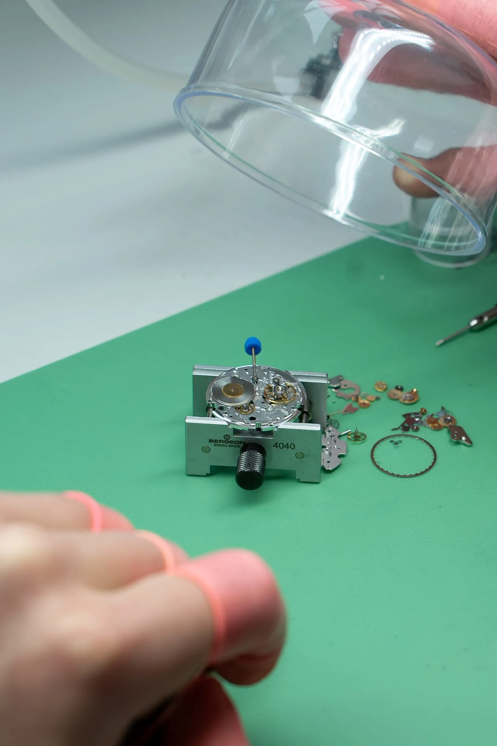 Watch movement in a holder with its parts laid out on the SwissMade bench
